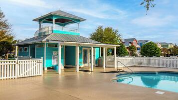 A turquoise lifeguard tower with a balcony, a covered seating area, and a pool.