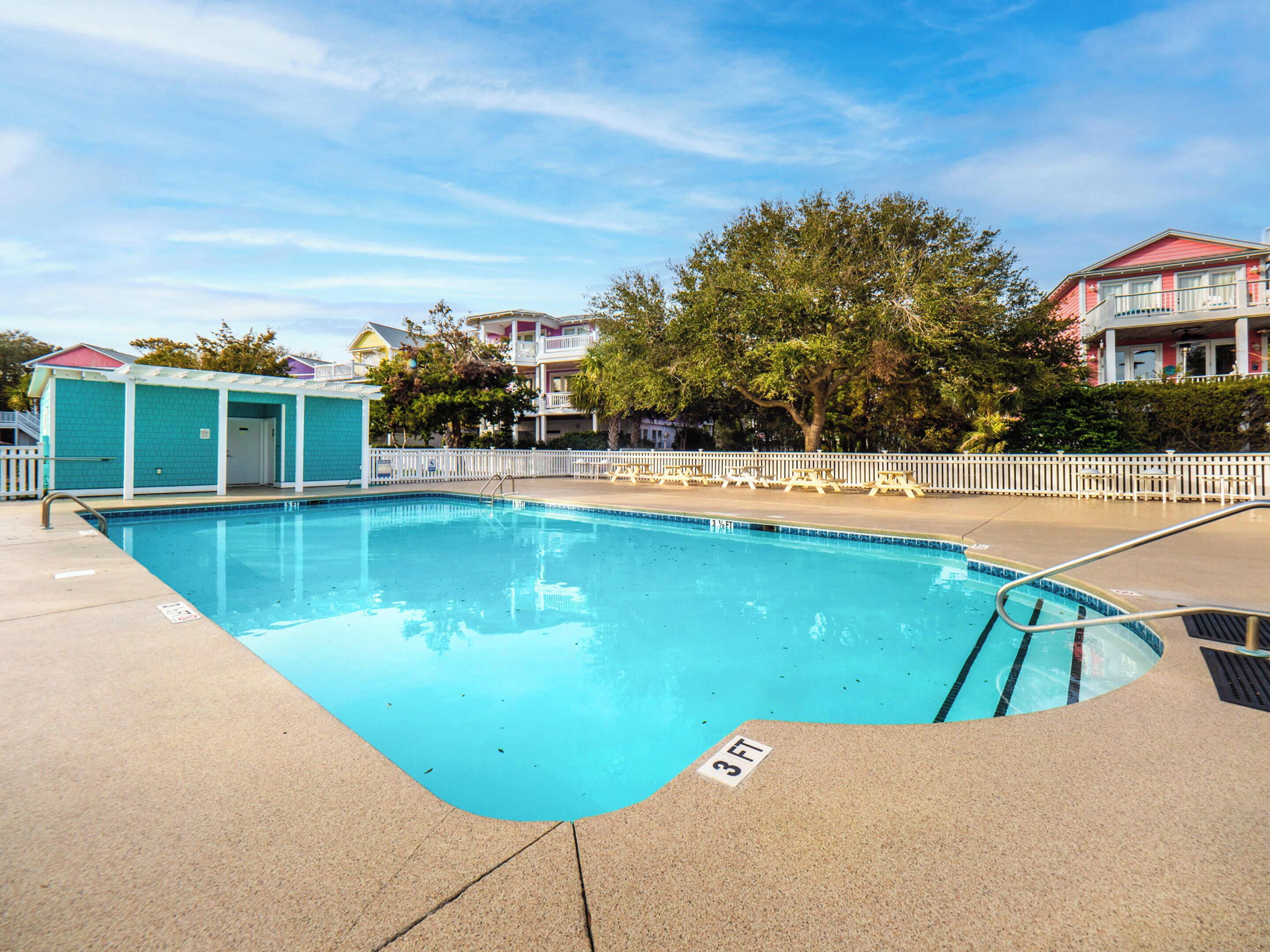A swimming pool with a 3 FT depth marker, surrounded by a white fence, with buildings and trees in the background.