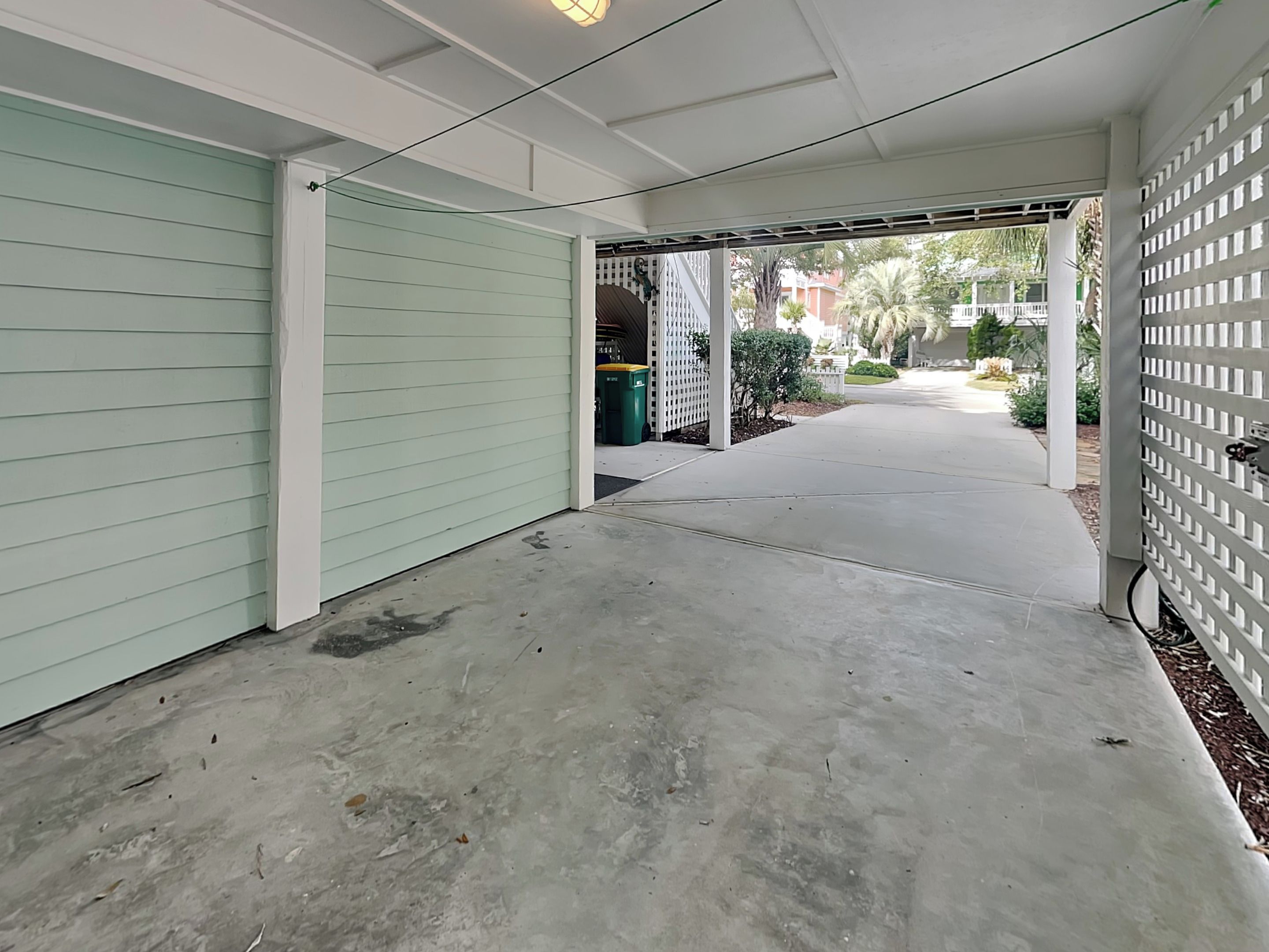A covered outdoor area with a concrete floor, a light green wall, and a white fence.