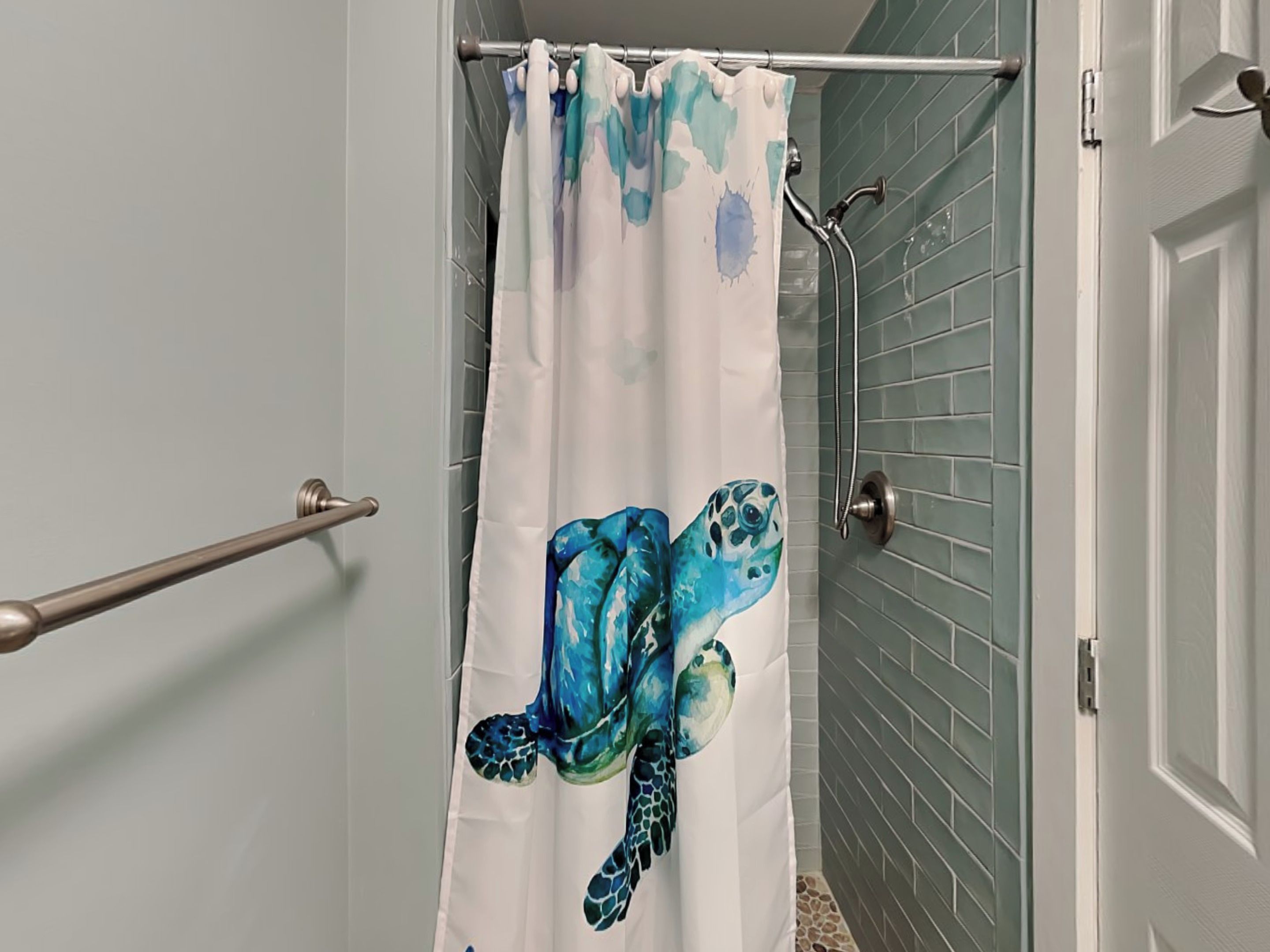 A bathroom with a shower curtain featuring a sea turtle design, a grab bar, and a door with a handle.