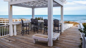 A wooden deck with a pergola, chairs, and a bench overlooking the ocean. - In Sea State Escape (Kure Beach)