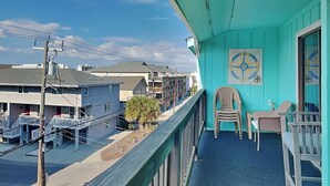 Un balcon turquoise donnant sur les maisons voisines, avec une chaise et une petite table.