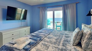Une chambre dotée d’un lit, d’un téléviseur à écran plat, d’un ventilateur de plafond et offrant une vue sur l’océan par le biais d’une porte coulissante.