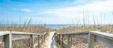 A wooden boardwalk leading to a beach with a clear sky.
