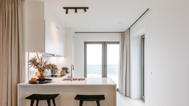 Eine moderne Küche mit Kochinsel, zwei Barhocker und Meerblick durch große Fenster.