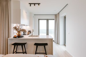 A modern kitchen with a central island, two bar stools, and a view of the sea through large windows. - The Sixteenth · Private Parking · Ostend (Oostende)