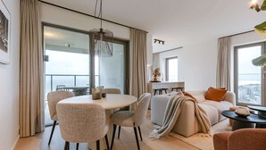 Ein modernes Wohnzimmer mit rundem Esstisch, gemütlicher Sitzgelegenheit, einer Couch und einem Balkon mit Blick auf die Stadt.