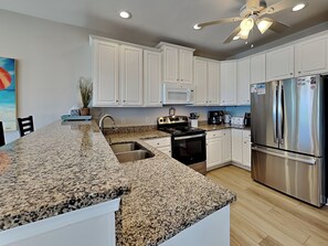 A kitchen with white cabinets, granite countertops, stainless steel appliances, and a ceiling fan. - Shore Is Something (Sneads Ferry)