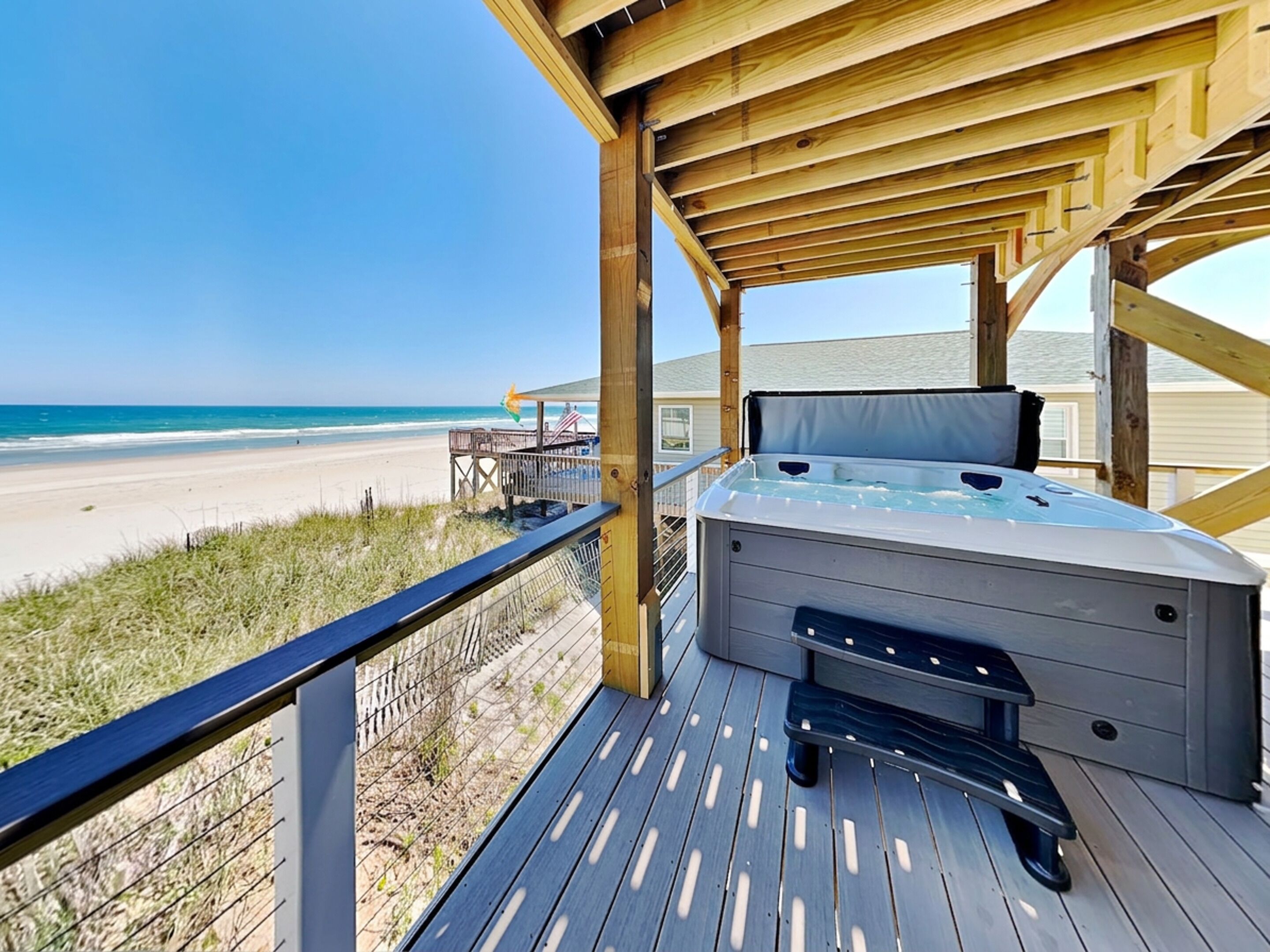 A wooden deck with a hot tub, overlooking a beach.