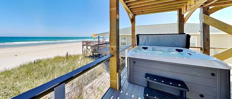 A wooden deck with a hot tub, overlooking a beach.