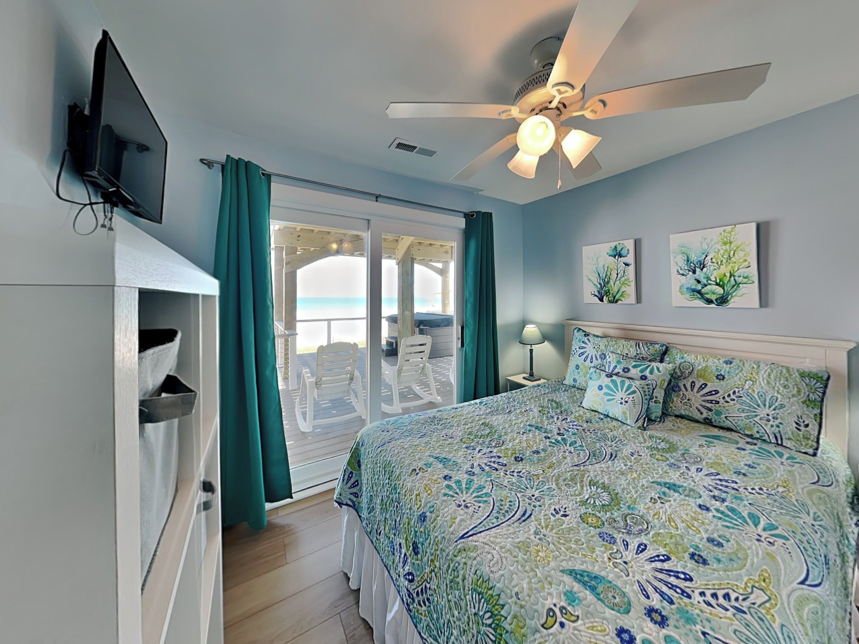 Une chambre avec un lit, un ventilateur de plafond, une tél évision et une vue sur la plage.