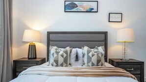 Un letto rifatto con cuscini decorati, due lampade da comodino e un quadro incorniciato al muro.