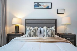 A neatly made bed with patterned pillows, two bedside lamps, and a framed artwork on the wall. - 4BR Pool Home at Storey Lake Near Disney (Kissimmee)