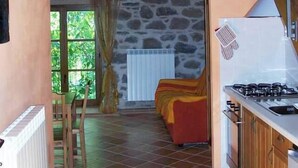 A rustic kitchen with a stone wall, wooden beams, and a red sofa in the background. - Ai Chiosi (Pontremoli)