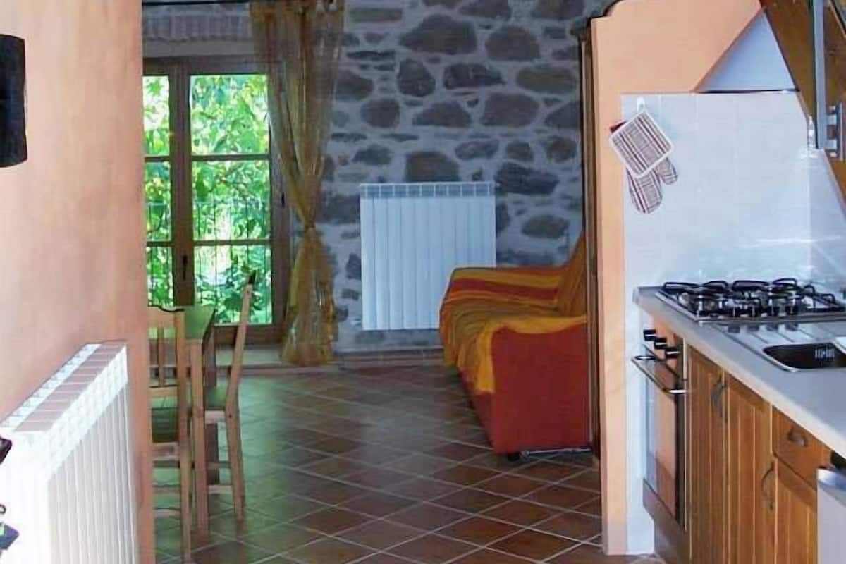A rustic kitchen with a stone wall, wooden beams, and a red sofa in the background.