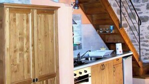 A rustic kitchen with wooden cabinets, a stove, and a stone wall in the background. - Ai Chiosi (Pontremoli)