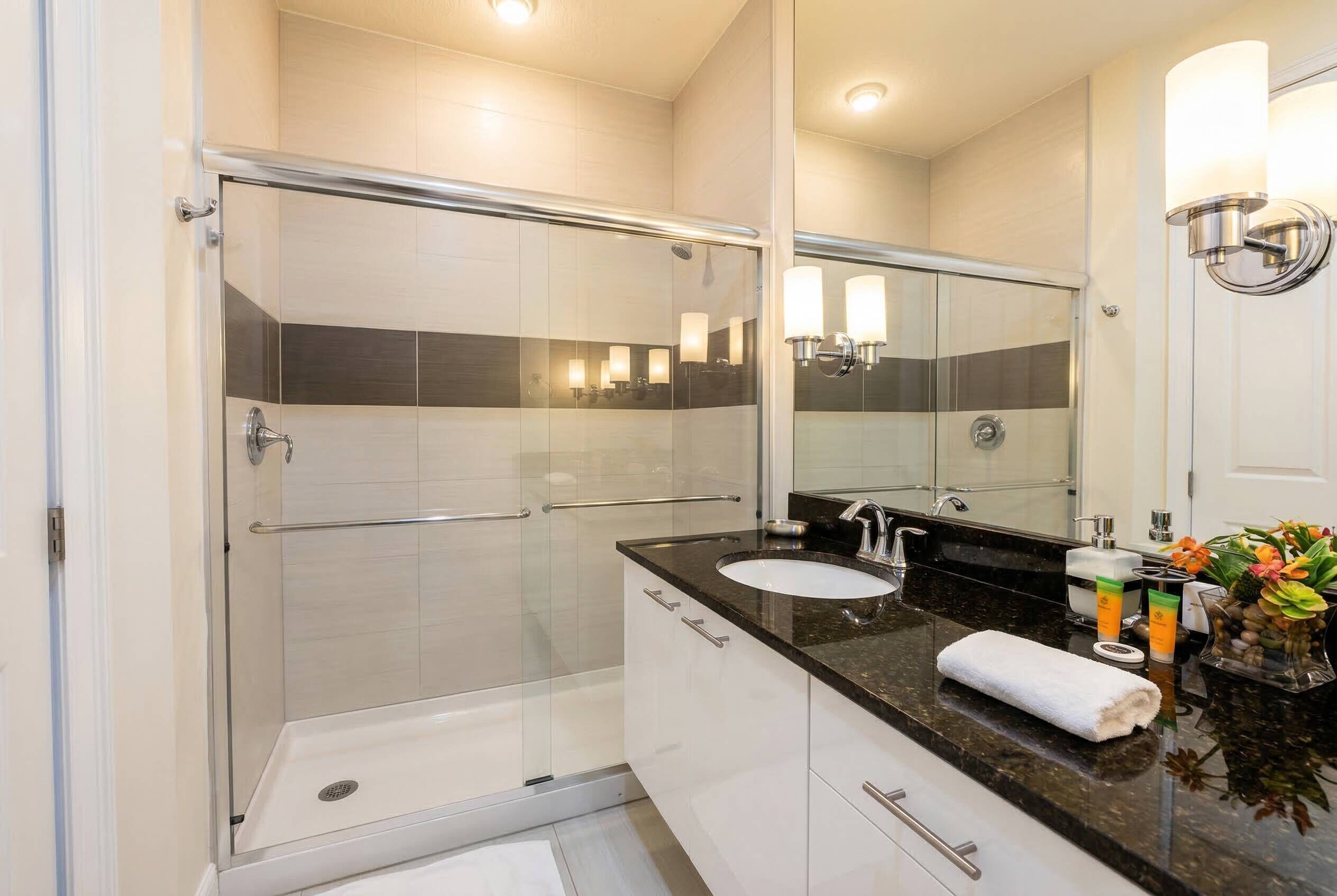 Un baño moderno con cabina de ducha de vidrio, un lavabo blanco y un espejo grande.