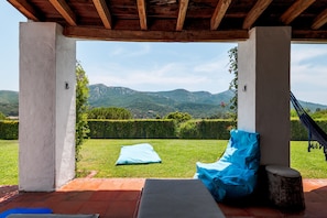 Un espace extérieur abrité avec des sièges, offrant une vue sur les montagnes, un hamac et un coussin bleu.