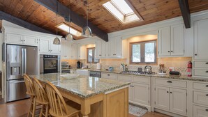 A spacious kitchen with white cabinets, a granite countertop island, wooden chairs, and a skylight. - Ski, Hike & Explore-Waitsfield Retreat Near Sugarbush (Waitsfield)