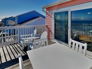 Una terraza con una mesa y sillas, una puerta de cristal que da a un balcón con vista al océano.