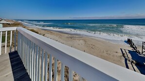 Vista sulla spiaggia da un pontile di legno con ringhiera, onde dell'oceano e cielo sereno.
