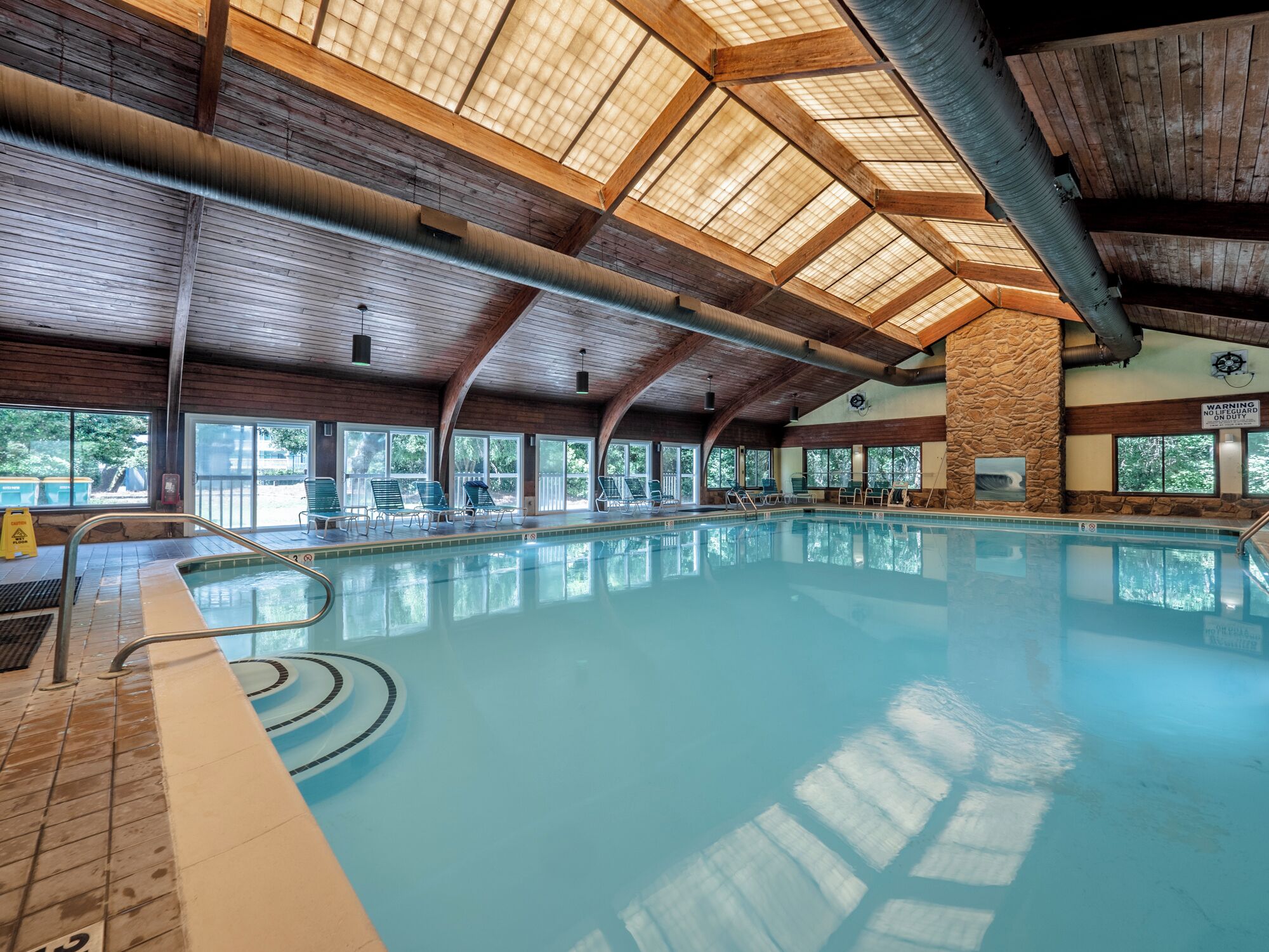 An indoor swimming pool with a high wooden ceiling and large windows.