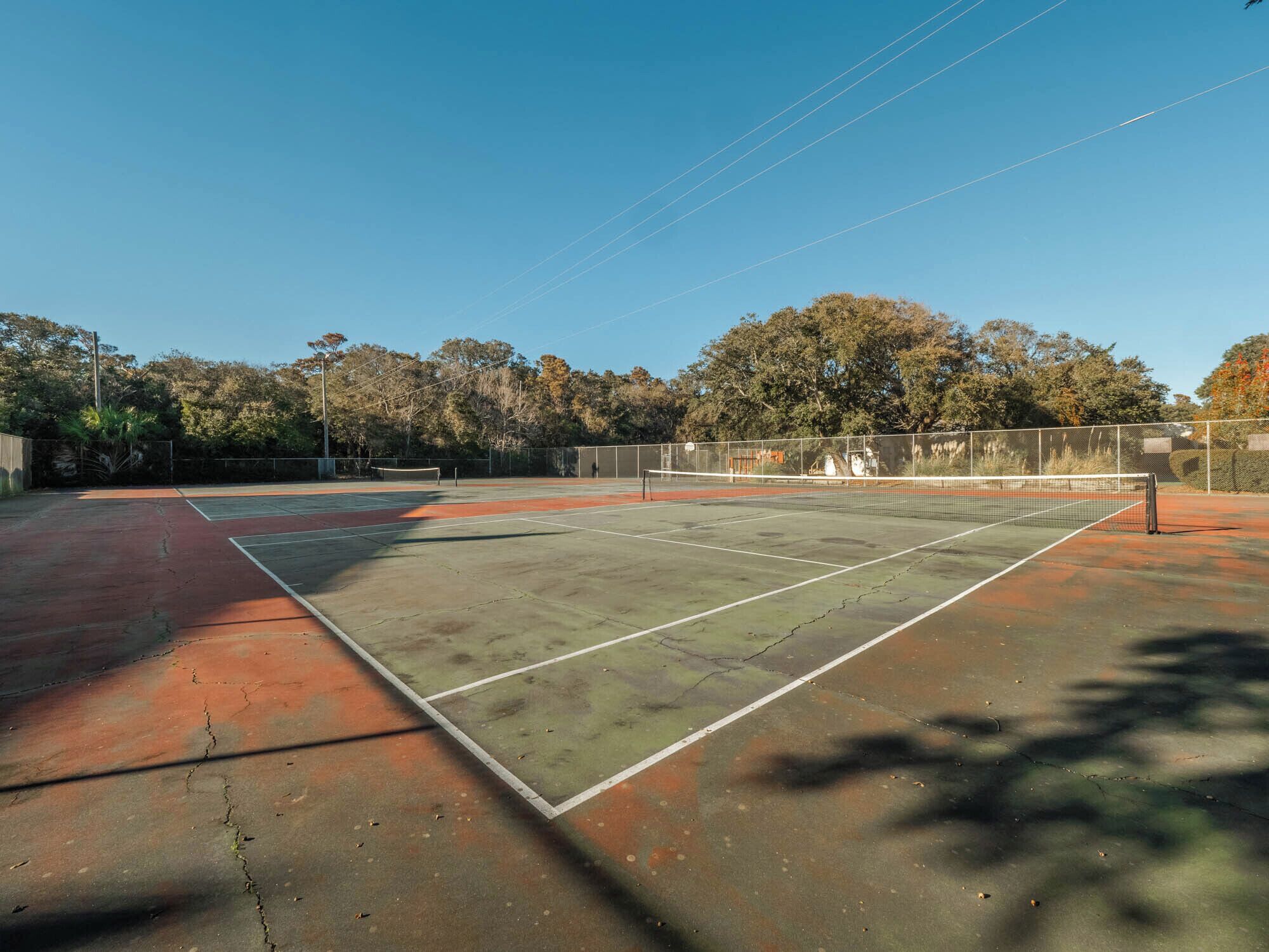 An outdoor tennis court with a net, surrounded by trees and a fence.