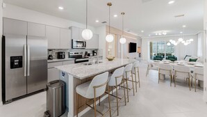 A modern kitchen with stainless steel appliances, a central island with bar stools, and a dining area with a large window. - Family 7BR Villa Near Disney & Parks (Clermont)