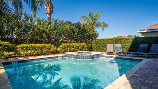 Ein Swimmingpool mit Whirlpool, umgeben von Palmen und einer Hecke, mit blauem Himmel darüber.