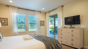 Ein Schlafzimmer mit einem Bett, einem Fernseher, einem Schminktisch und einem Fenster mit Vorhängen.