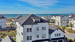 A coastal residential area with white houses, a clear blue sky, and a view of the ocean. - Sand & Stories: Rooftop Deck, Pet-Friendly, Sleeps 16, Sugar Sands Community (Mexico Beach)