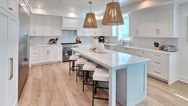 A modern kitchen with white cabinetry, a central island with bar stools, and pendant lighting. - Sand & Stories: Rooftop Deck, Pet-Friendly, Sleeps 16, Sugar Sands Community (Mexico Beach)