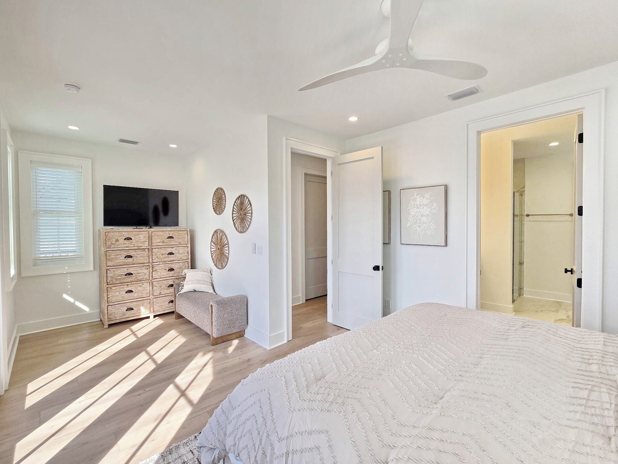 Un dormitorio con cama, cómoda, televisor y puerta que da a un baño.