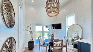 A dining area with a round table, chairs, a chandelier, and a view through the glass door. - Sand & Stories: Rooftop Deck, Pet-Friendly, Sleeps 16, Sugar Sands Community (Mexico Beach)