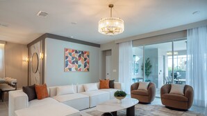 A modern living room with a sectional sofa, two armchairs, a coffee table, and a chandelier. - Luxury 7BR 7BA House w Private Pool Disney (Kissimmee)