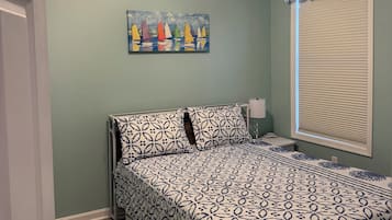 A bedroom with a bed, a ceiling fan, a painting, a window with blinds, and a door.
