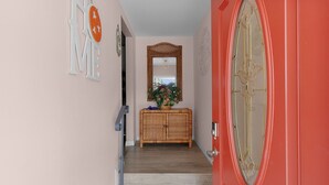 A hallway with a red door, a wicker console table with a basket, and a mirror above it. - Lake Paradise 2B/2B Home in Village of Orange Blossom Gardens (The Villages)