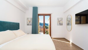 Hotellihuone, jossa on suuri sänky, lasiovesta avautuva näkymä kaupunkiin ja taideteoksia seinillä.