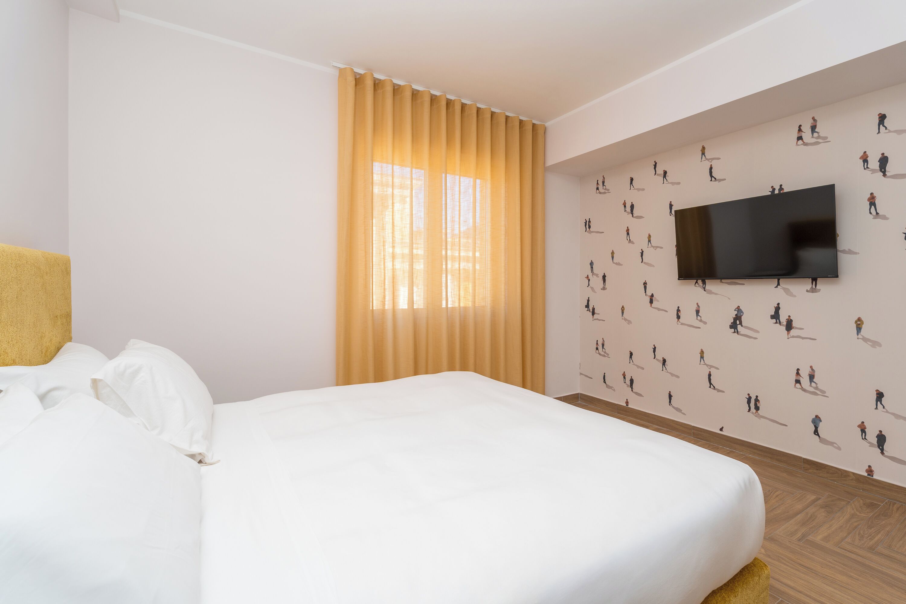 Una camera d'albergo con un letto, una TV a muro e una finestra con tende.