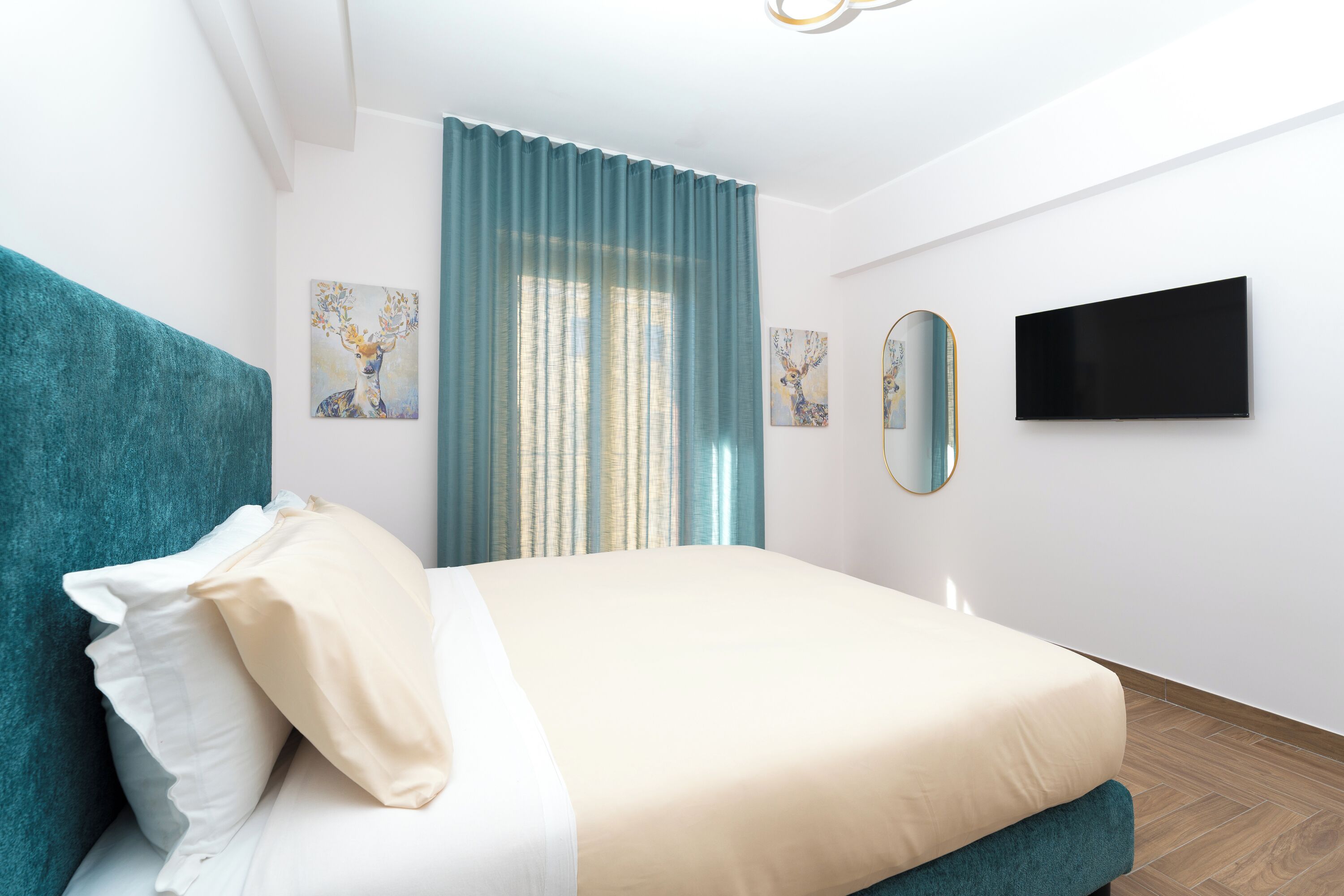 Um quarto moderno com cama, cabeceira azul-turquesa, roupa de cama branca e obras de arte nas paredes.