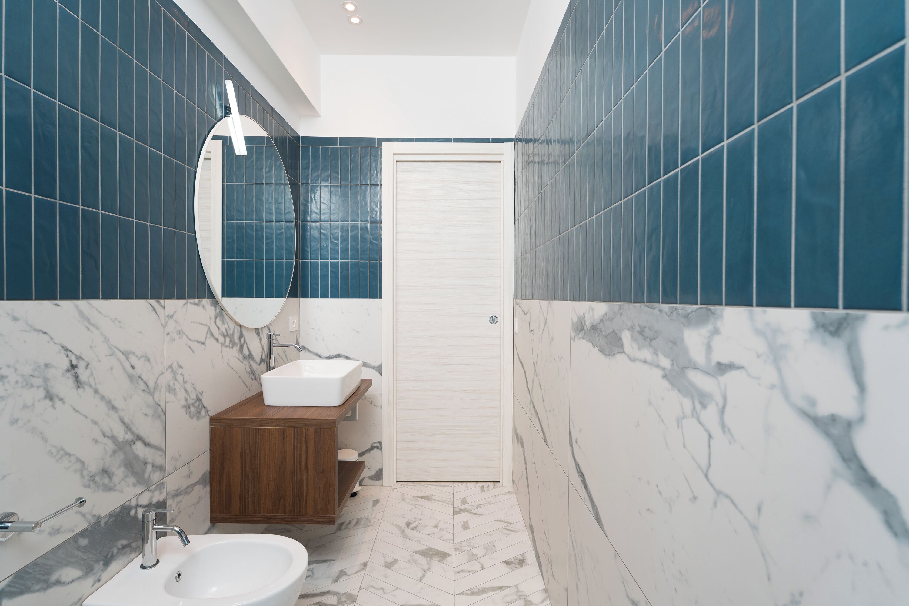 Un bagno moderno con lavandino bianco, mobile in legno e specchio.