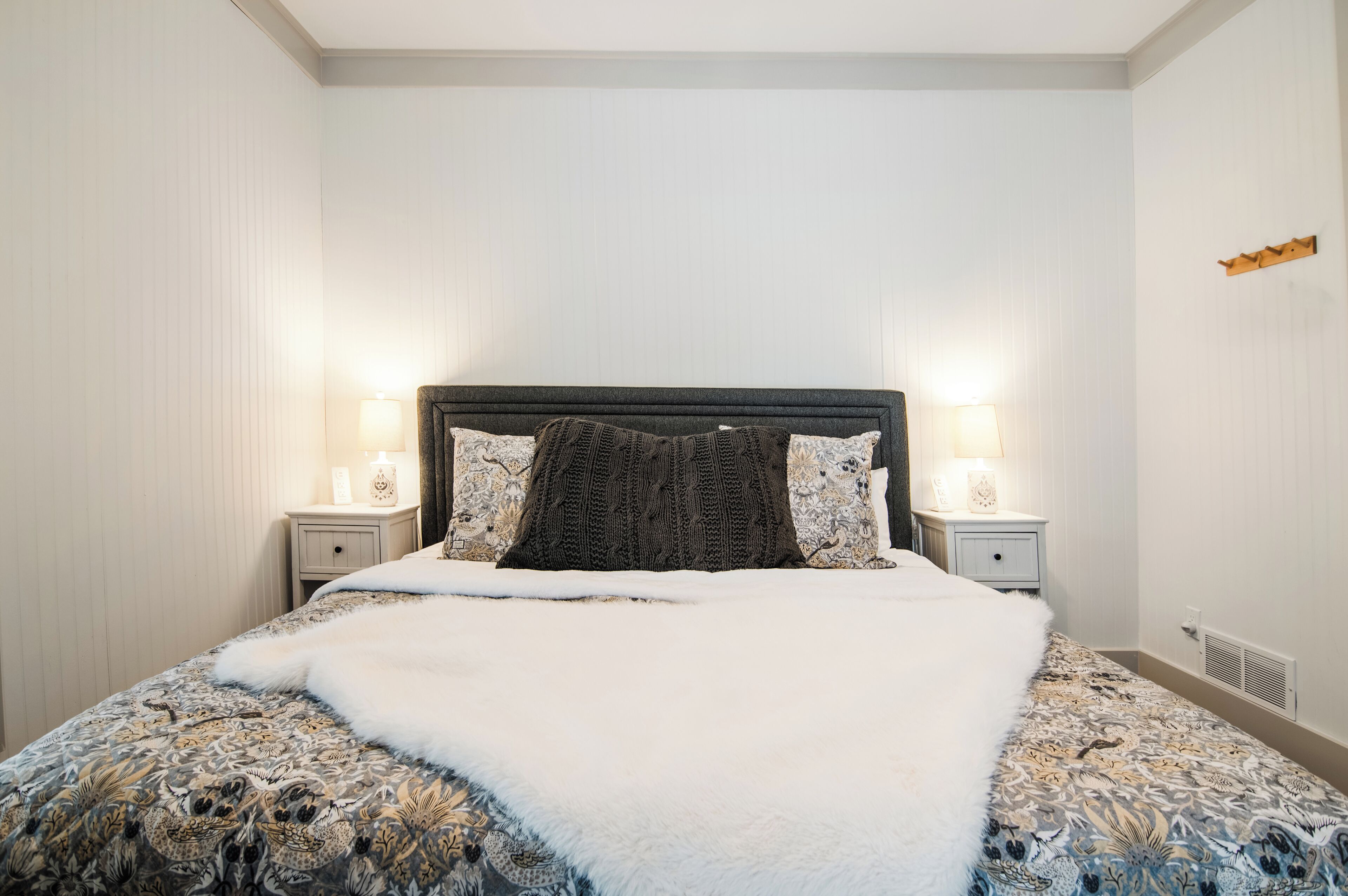 A neatly made bed with a patterned bedspread and a white throw blanket, flanked by two bedside tables with lamps.