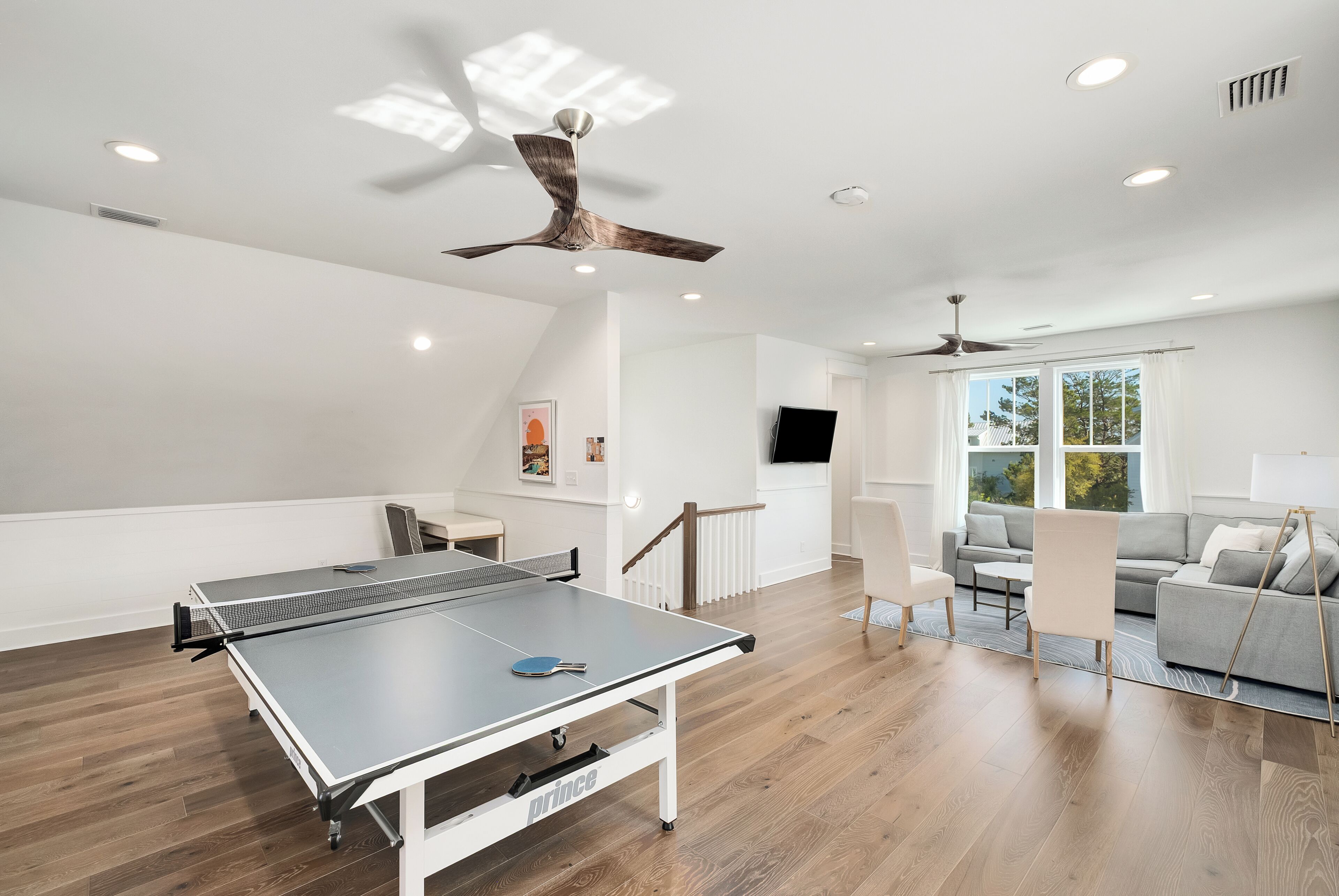 A spacious room with a ping pong table, ceiling fans, a TV, and a sofa.