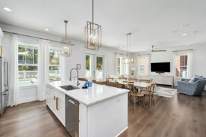 Une cuisine spacieuse dotée d’un îlot central, de planchers en bois et de luminaires suspendus.