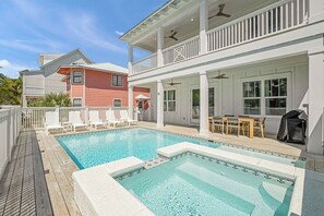 A swimming pool with a wooden deck, a covered patio with outdoor furniture, and a two-story house with a balcony. - Sunny Side Up | Private Pool/Spa | 6-Seater Golf Cart | Walk to Beach (Santa Rosa Beach)