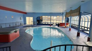 An indoor swimming pool with a curved design, surrounded by a blue and red wall, and a seating area with chairs and tables. - 2 bedroom lakefront condo at The Lake of the Ozarks (Lake Ozark)