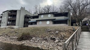 A multi-story building with balconies, a river in front, and a wooden bridge. - 2 bedroom lakefront condo at The Lake of the Ozarks (Lake Ozark)