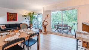 A modern dining area with a wooden table set for four, a black sofa, and a large window with a view of greenery. - Fleur de Sel - Centre de Nantes avec parking (Nantes)