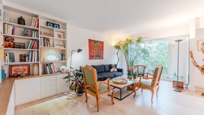 A modern living room with a sofa, wooden chairs, a coffee table, and a bookshelf filled with books and decorative items. - Fleur de Sel - Centre de Nantes avec parking (Nantes)