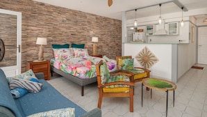 A bedroom with a bed, a sofa, a chair, a small table, a ceiling fan, and a kitchenette. - Le Ti Mahogany - Studio avec Balcon (Saint-Francois)